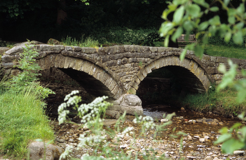 DCP0564 
 800 year old Pack-Horse Bridge at Wycoller in Lancashire also known as Sally's Bridge, crossing Wycoller beck. 
 Keywords: horizontal, ancient, old, span, architecture, archway, arch, framed, frame, green, foliage, pebble, dry, stream, Beck, water, river, stone, Sally, heritage, historic, history, bridge, horse, pack, park, country, Trawden, Wycoller, Europe, Britain, UK, England, Northwest, West, North, Lancs, Lancashire