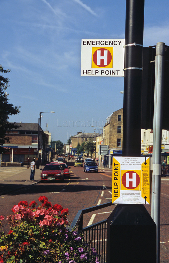 DCP0529 
 Help point in Colne town centre 
 Keywords: Lancashire, Lancs, North, West, Northwest, England, UK, Britain, Europe, Colne, Town, Centre, help point, help, cctv, crime, prevention, lamp, post, info, information, intercom, contact, red, circle, call for help, flower, box, road, transport, car, shop, shopping, business, commerce, trade, traffic light, vertical
