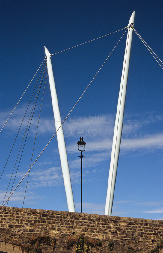 DCP0549 
 Detail of the Millennium Bridge in Lancaster part of the National Cycle Network. Designed by Whitby Bird Architects the bridge was opened in 2001 
 Keywords: Lancashire, Lancs, North, West, Northwest, England, UK, Britain, Europe, Lancaster, city, millenium, bridge, 2001, millenium, detail, part, architecture, strut, support, post, supension, lamp, light, illumination, illuminate, wall, abstract, pattern, contrast, old and new, ancient and modern, modern, blue, sky, cloud, triangle, shape, v, line, vertical