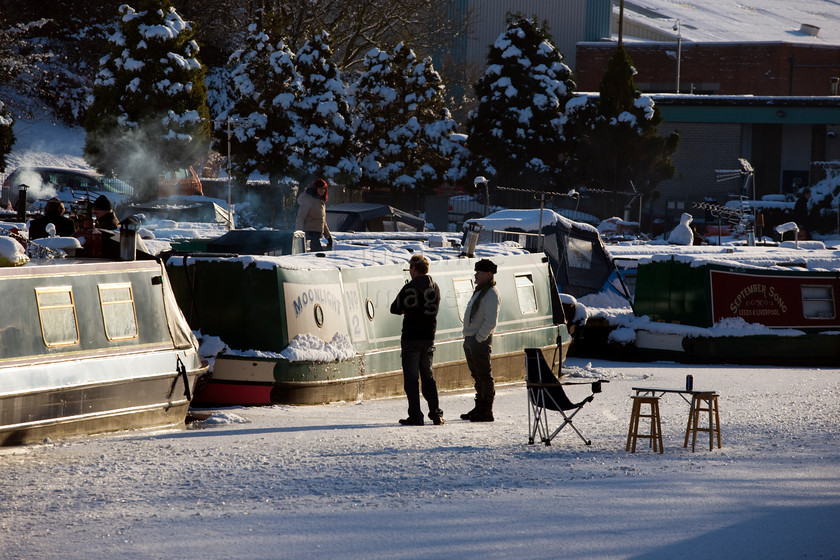 DCP1718 
 Narrow boats and people standing on frozen Leeds and Liverpool canal at Adlington 
 Keywords: Adlington, Leeds and Liverpool, Canal, waterway, season, winter, snow, cold, ice, freeze, frozen, people, table, chair, narrow, boat, barge, transport, transportation, moored, shadow, shadows, blue, sky, Lancashire, Lancs, Northwest, North, West, England, UK, Britain, Europe, DCP1718